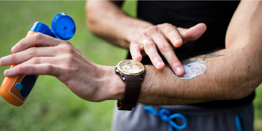 #PraTodosVerem: A imagem é focada no braço de um homem que usa relógio enquanto passa protetor solar.